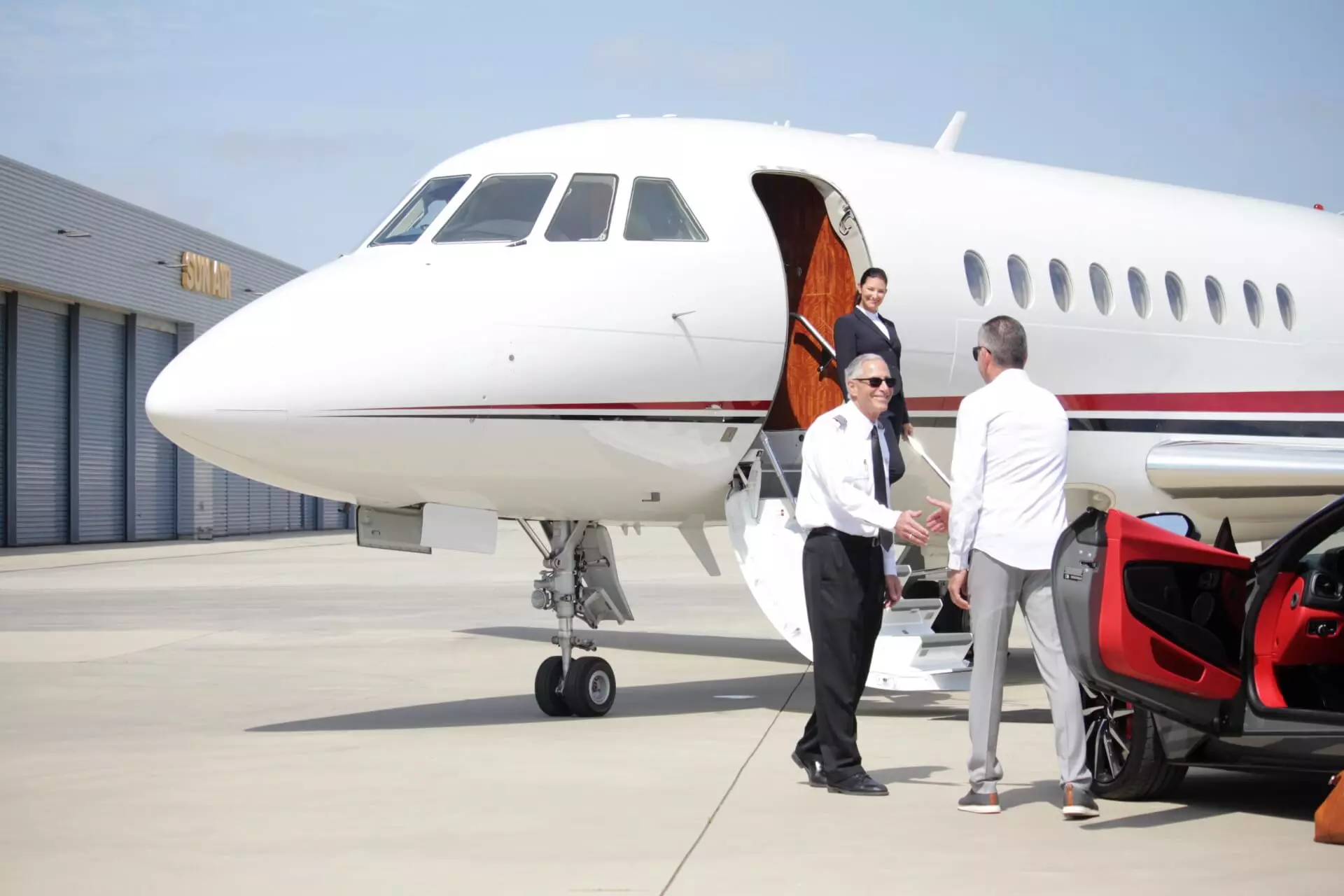 People exiting a vehicle greeting a pilot of a private jet